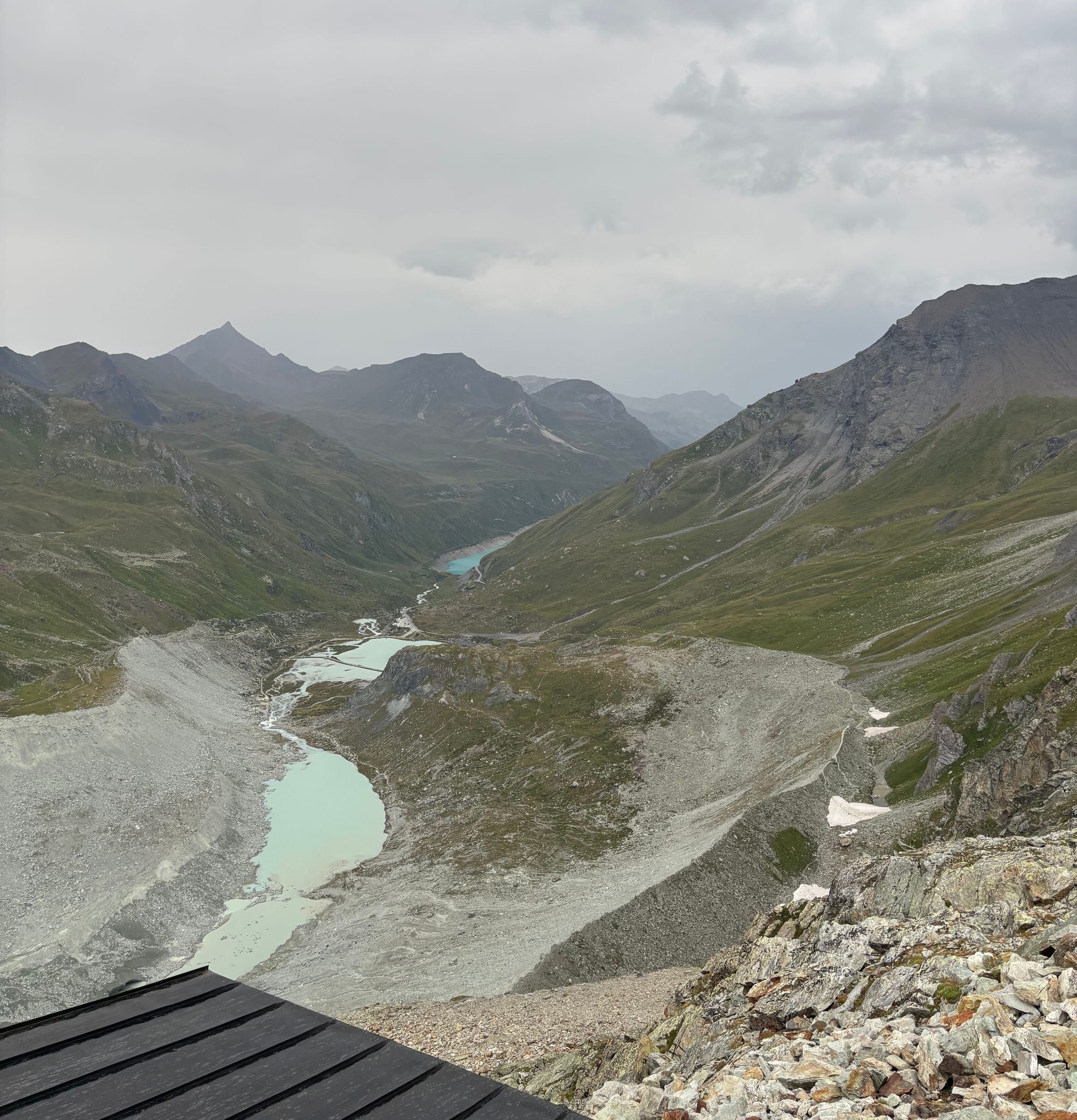 View from the Moiry hut over the glacial valley, the turquoise Lac de Châteaupré and the moraine, under a grey sky